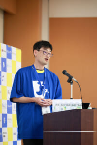 写真 青いシャツを着て PyCon JP 2024 登壇中の西本